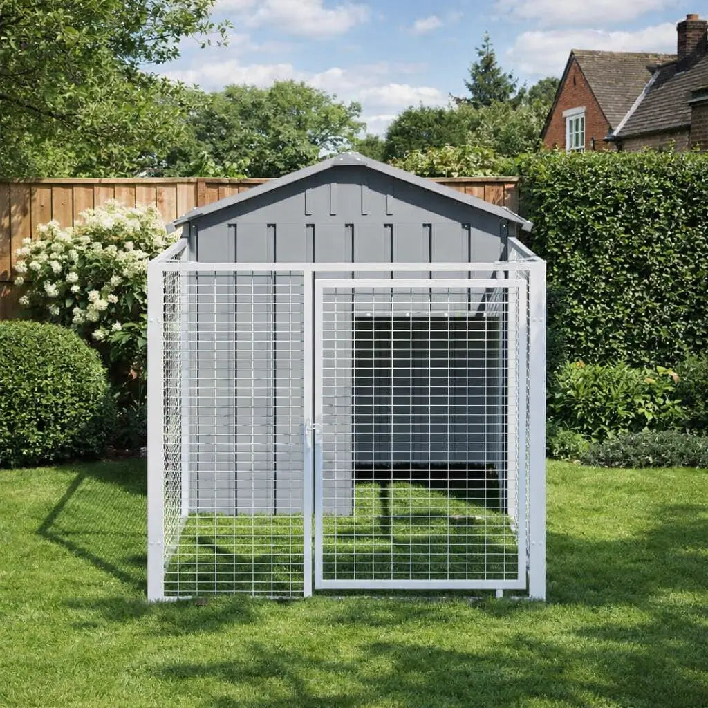 Outdoor galvanised steel dog kennel with run placed on lawn in garden setting with fence and hedges